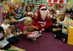 Dzieci siedzą z Mikołajem w kole, trzymają w rękach książeczki.